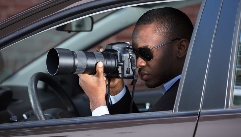 Private Detective Sitting Inside Car Photographing With SLR Camera