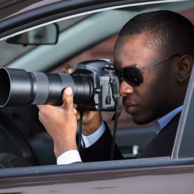 Private Detective Sitting Inside Car Photographing With SLR Camera