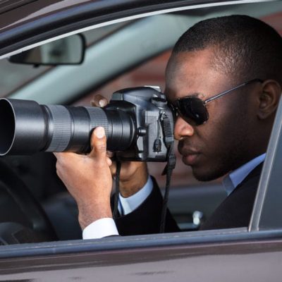 Private Detective Sitting Inside Car Photographing With SLR Camera